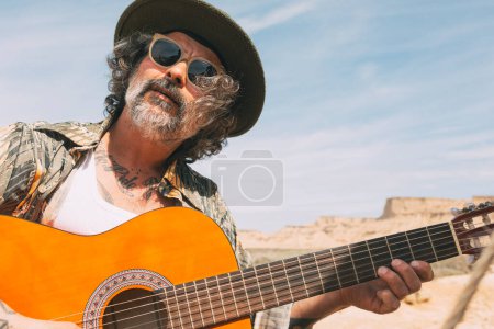 Photo for Free traveling young hipster man playing the guitar while traveling in the mountains. Country music - Royalty Free Image