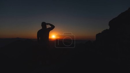 Téléchargez les photos : La silhouette d'un homme libre debout et regardant le beau coucher de soleil seul sur le sommet de la montagne. - en image libre de droit