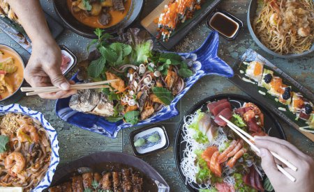 Téléchargez les photos : Mains avec baguettes manger thaï nourriture fermer, salades et wok, nourriture asiatique, vue sur le dessus. Cuisine japonaise et thaïlandaise. - en image libre de droit