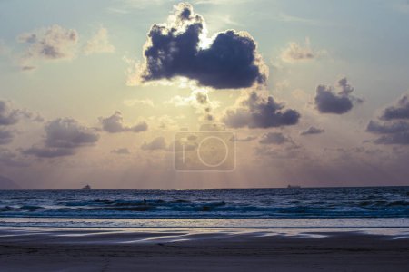 Téléchargez les photos : Un grand nuage est dans le ciel au-dessus de l'océan. Le soleil se couche, projetant une lueur chaude sur l'eau. Le ciel est rempli de nuages, créant une atmosphère lunatique - en image libre de droit
