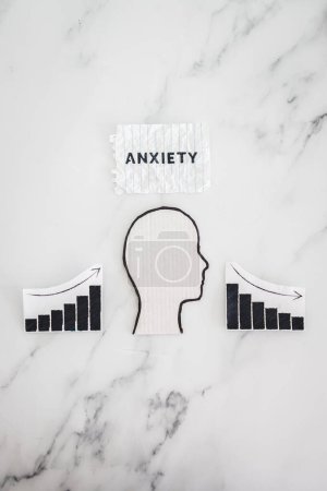 Photo for Mental health and mood swings conceptual image, cardboard head with Anxiety text on scrunched up torn paper with graphs showing stats going up and down - Royalty Free Image