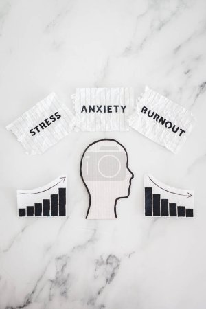 Photo for Mental health and mood swings conceptual image, cardboard head with Stress Anxiety and Burnout texts on scrunched up torn papers with graphs showing stats going up and down - Royalty Free Image