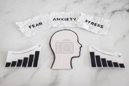 Photo for Mental health and mood swings conceptual image, cardboard head with Fear Anxiety Stress texts on scrunched up torn paper with graphs showing stats going up and down - Royalty Free Image