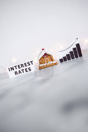 Photo for Cost of living and inflation rising around Christmas 2022, gingerbread house next to interest rates graph with stats going up and fairy lights in the background - Royalty Free Image