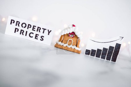 Photo for Cost of living and interest rates rising around Christmas 2022, gingerbread house next to property prices graph with stats going up and fairy lights in the background - Royalty Free Image