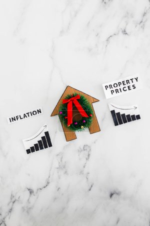 Photo for Graphs with inflation going up and property prices going down next to cardboard house with festive wreath, concept of post pandemic economy during winter 2022 - Royalty Free Image