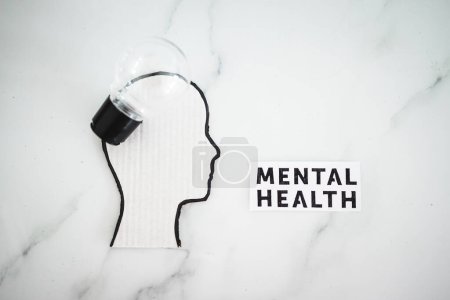 Foto de Texto de salud mental junto a la cabeza de cartón con bombilla, concepto de psicología - Imagen libre de derechos