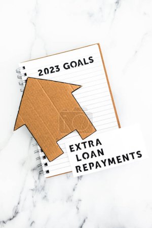 Foto de New year 2023 goals on notebook with cardboard house and extra loan payments text, concept of financial independence and being free from debt - Imagen libre de derechos