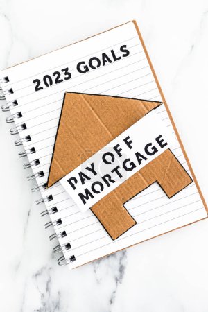 Foto de New year 2023 goals on notebook with cardboard house and Pay Off Mortgage text, concept of financial independence and being free from debt - Imagen libre de derechos