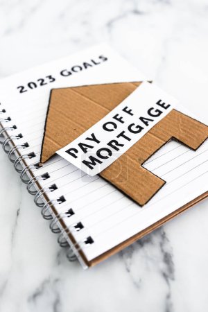Foto de New year 2023 goals on notebook with cardboard house and Pay Off Mortgage text, concept of financial independence and being free from debt - Imagen libre de derechos