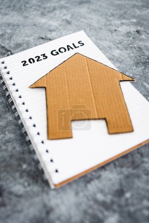 Foto de Concept of buying a house or settling down, 2023 goals on notebook with cardboard house - Imagen libre de derechos