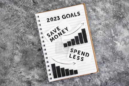 Téléchargez les photos : Spend less and save money texs with graphs showing expenses going down and savings going up on 2023 goals notebook, concept of financial stability and being free from debt - en image libre de droit