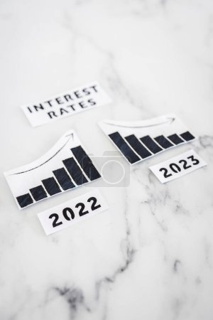 Photo for Interest rates text with 2022 chart showing stats increasing and 2023 graph showing stats decreasing, concept of economy recovering in the new year - Royalty Free Image