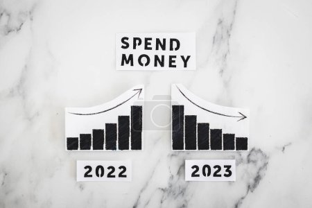 Photo for Spend money text with 2022 chart showing stats increasing and 2023 graph showing stats decreasing, concept of consumer spending going down in the new year - Royalty Free Image