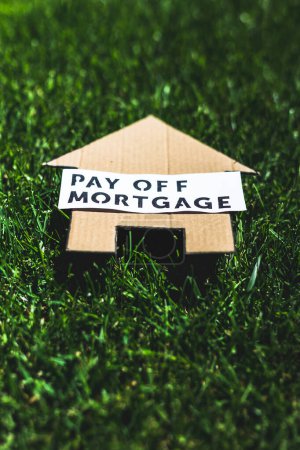 Foto de Financial independence and being free from debt, Pay Off Mortgage text over cardboard house on perfect green lawn shot under strong sunshine - Imagen libre de derechos