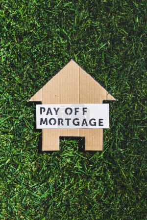financial independence and being free from debt, Pay Off Mortgage text over cardboard house on perfect green lawn shot under strong sunshine