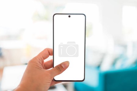 Photo for Hand holding smartphone with copy space in front of stylish living room home interior background, shot at shallow depth of field - Royalty Free Image