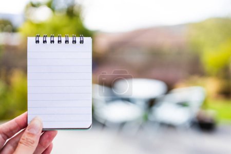 Photo for Hand holding small notepad with blank copy space in front of stylish backyard patio background, space to add your text - Royalty Free Image