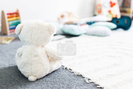 weißer Teddybär von hinten gesehen in schönen fröhlichen und chaotischen Kinderzimmer oder Kinderzimmer mit bunten Holzspielzeug und weichen Kissen und Teppichen, Kindheit lernen und Wohnkultur-Konzepte