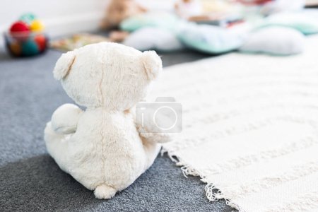 white teddy bear seen from behind in beautiful happy and messy nursery or children's room with colorful wooden toys and soft pillows and rugs, childhood learning and home decor concepts