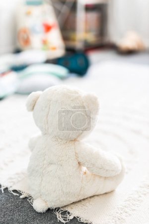 weißer Teddybär von hinten gesehen in schönen fröhlichen und chaotischen Kinderzimmer oder Kinderzimmer mit bunten Holzspielzeug und weichen Kissen und Teppichen, Kindheit lernen und Wohnkultur-Konzepte
