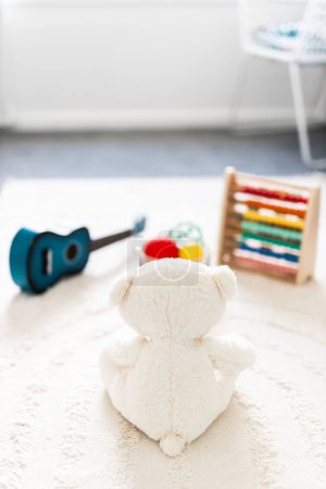white teddy bear seen from behind in beautiful happy and messy nursery or children's room with colorful wooden toys and soft pillows and rugs, childhood learning and home decor concepts