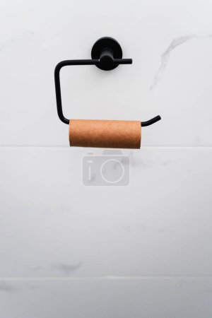 leere Toilettenpapierrolle auf schwarzem Rollenhalter auf weißem Marmor geflieste Wand, Humorbild über auslaufendes Toilettenpapier oder Darmprobleme