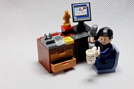 Photo for Osaka, Japan - February 19, 2023 Lego businessman sits at his working table with computer, trophy, cup and telephone receiver on white dot color background. - Royalty Free Image