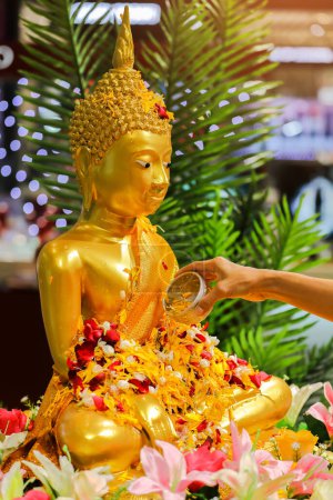 Nahaufnahme einer Frau, die am Songkran Festival Day in Thailand Wasser auf ein goldenes Buddha-Bild streut.
