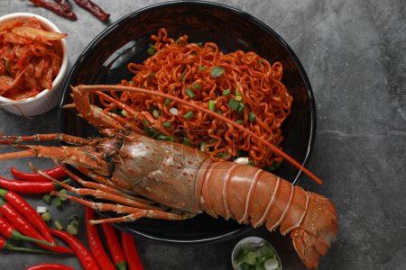 Téléchargez les photos : Top vue nouilles instantanées séchées épicées coréennes avec homard épineux peint et kimchi sur fond de table noire. Concept des aliments asiatiques. - en image libre de droit