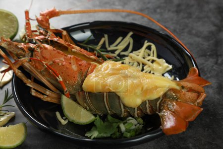 Téléchargez les photos : Gros plan du homard épineux peint cuit au four avec du fromage sur fond de table noire. Concept de fruits de mer. - en image libre de droit