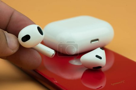 Photo for Bangkok, Thailand - November 19, 2022 : Man hand holding Apple AirPods 3 with red Iphone. Close up - Royalty Free Image