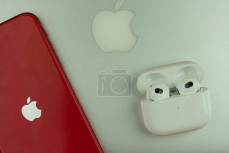Photo for Bangkok, Thailand - November 28, 2022 : New Apple AirPods 3 and charging case next to iPhone 11 product red model place on MacBook pro. Top view - Royalty Free Image