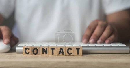 Kontaktwort geschrieben auf Holzblock mit Mann und Tastatur. Technischer Support Center Kundendienst Geschäftskonzept