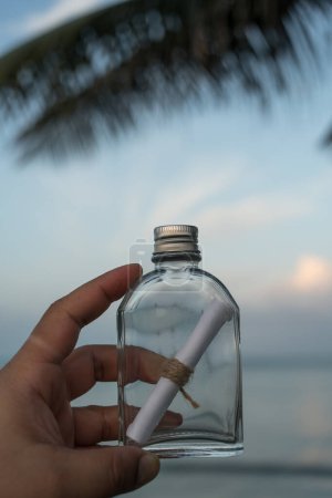 Photo for Message in glass bottle on hand with sea background - Royalty Free Image