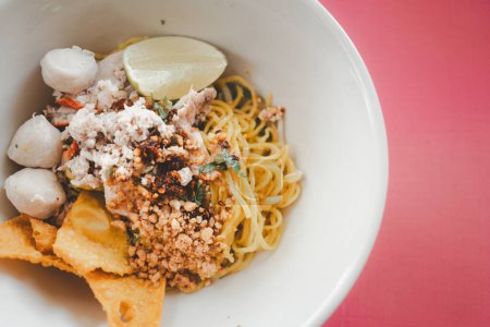Egg noodles dried egg noodles with lime, minced pork, meatballs, and fried dumplings in white bowl. Asian food style