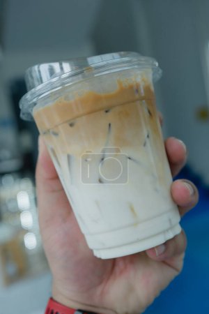 Téléchargez les photos : Café latte glacé frais, le fond comme dessus de lait par le café tourné dans un verre en plastique à portée de main - en image libre de droit
