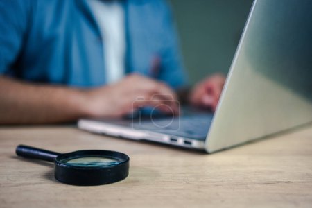 Téléchargez les photos : Un homme d'affaires travaille sur un ordinateur avec une loupe sur la table. concept d'analyse des données. Recherche d'informations ou de preuves - en image libre de droit
