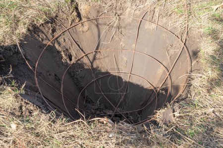 A hole with iron basket in it for tree soil lump forming dug with specialized spade machine for transplanting and transport trees. Landscaping, seasonal agricultural engineering, large trees landing machines.
