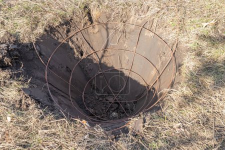 A hole with iron basket in it for tree soil lump forming dug with specialized spade machine for transplanting and transport trees. Landscaping, seasonal agricultural engineering, large trees landing machines.