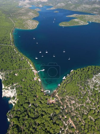 Drone aerial view of yachts and boats at wooden pier and in dark blue waters of Telascica bay in National Park, Croatia