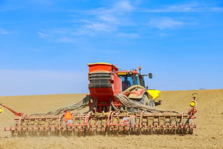 Foto de La maquinaria agrícola trabaja durante la temporada de trabajo del campo de primavera. Un tractor con una sembradora en el campo siembra cereales. Negocio agroindustrial. - Imagen libre de derechos