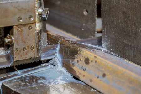 Foto de Corte de perfiles y tuberías de acero en una sierra de cinta en producción. - Imagen libre de derechos