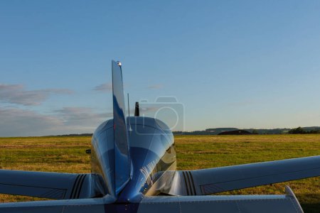 Photo for A small 2-seater plane against a blue sky with white clouds. Back view. Airplane on the field with grass. - Royalty Free Image