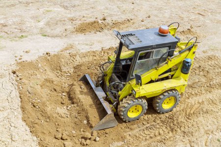 Una mini cargadora de tractores se mueve y carga tierra en un sitio de construcción. Nivelación de la superficie del terreno antes de la construcción.