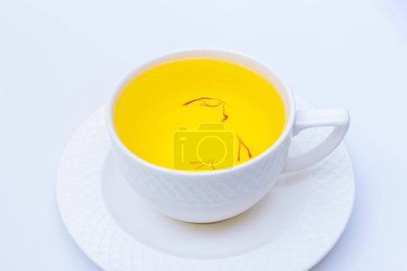 Foto de Té de azafrán en una taza blanca sobre un fondo blanco. Una bebida saludable fragante. - Imagen libre de derechos
