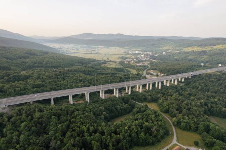Transport bridge in mountainous area, road and trees. Light fog in the mountains. Development of transport systems. A panoramic view of nature from above.