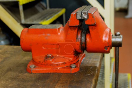 Téléchargez les photos : L'étau est fixé sur l'établi de travail des métaux. Un étau rouge sur un établi en bois dans une usine de métallurgie. Outils de banc. - en image libre de droit