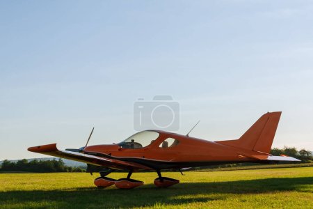 Photo for A small 2-seater plane against a blue sky with white clouds. Back view. Airplane on the field with grass. - Royalty Free Image