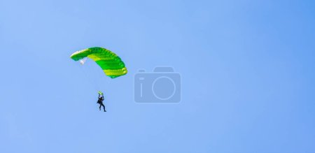 Photo for A parachutist with a light green parachute canopy against a background of blue sky and white clouds. Parachute jumping. - Royalty Free Image